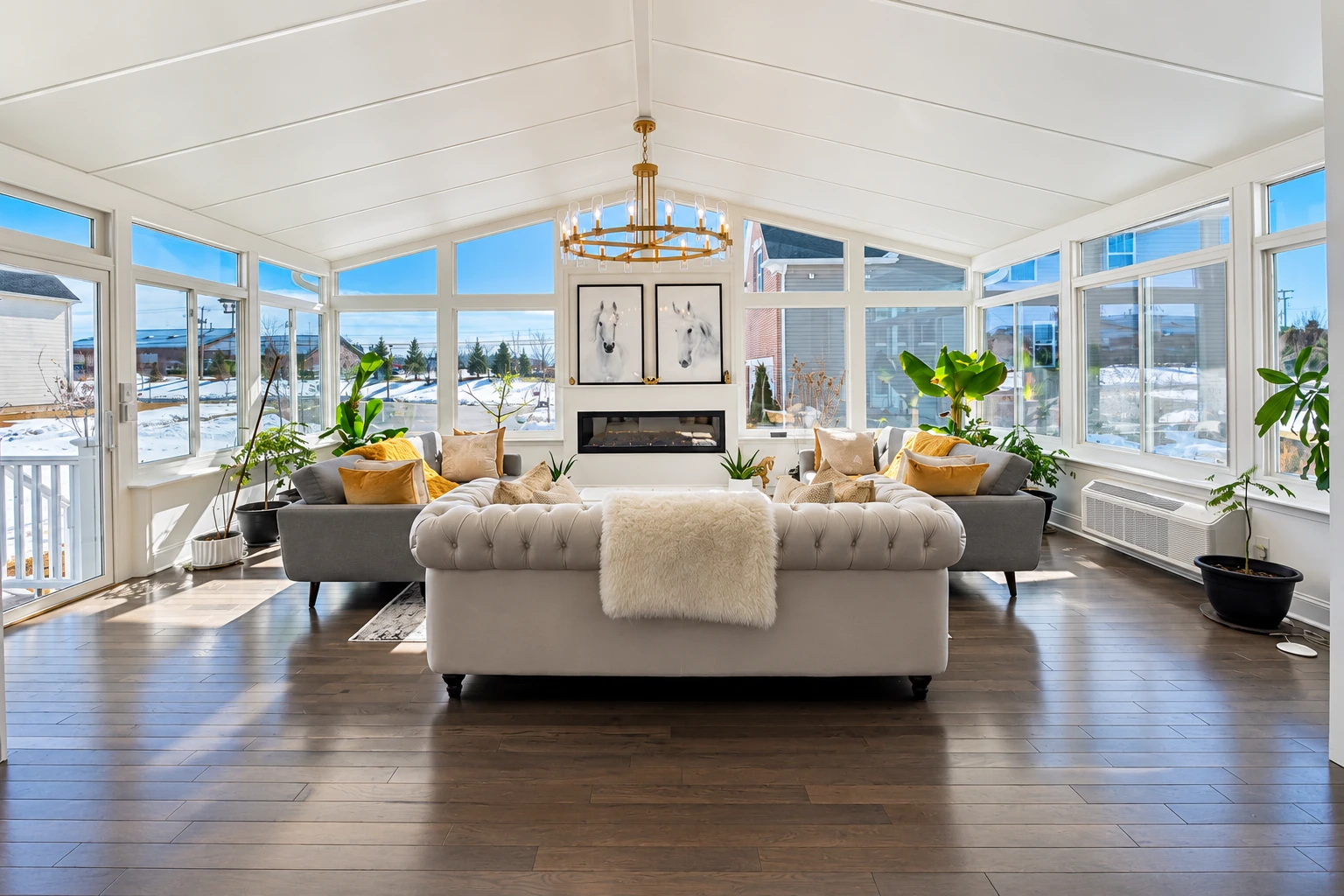 Custom sunroom with white-framed windows, a vaulted ceiling, fireplace, chandelier, and seating on dark wood floors.