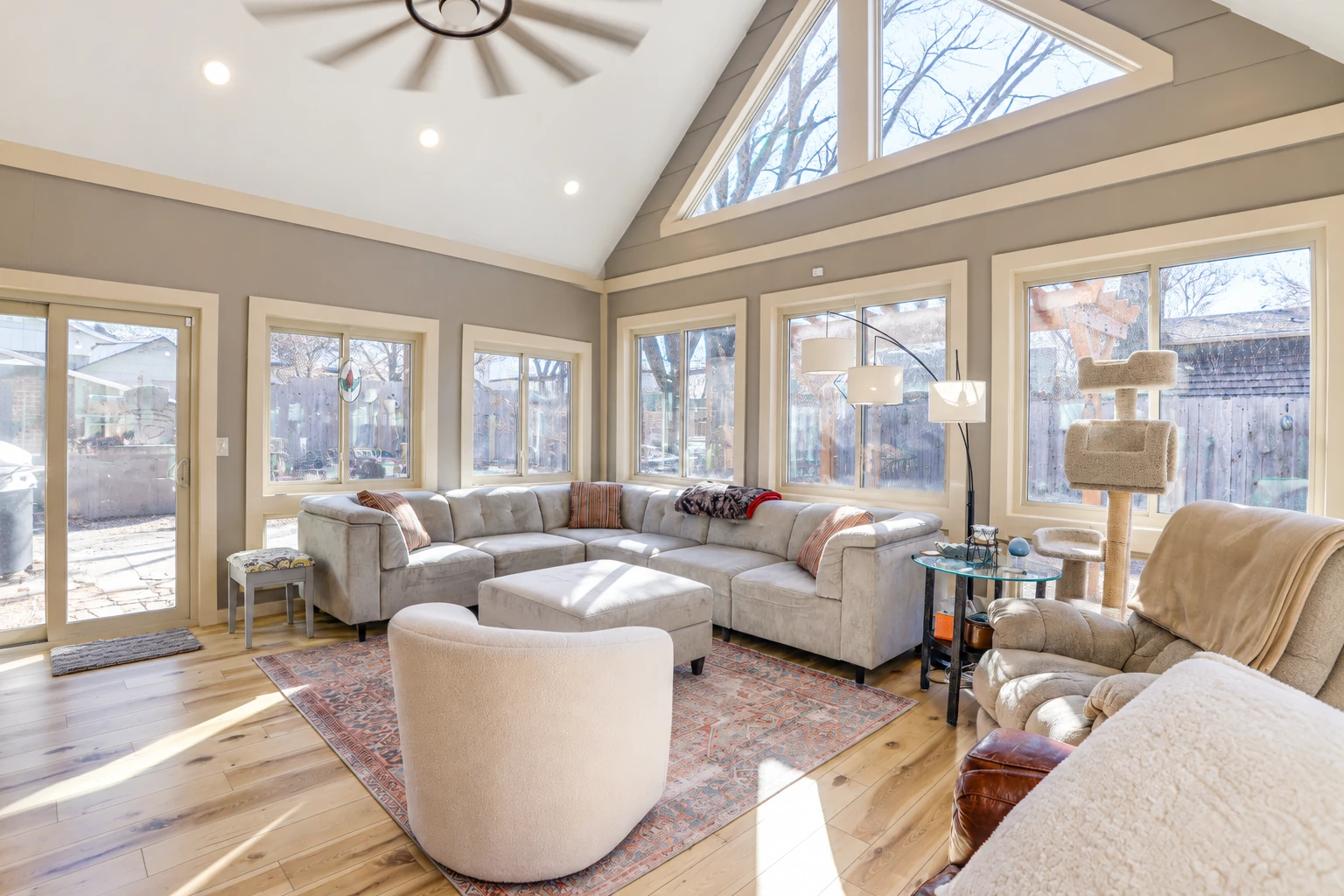 Bright vinyl sunroom with a vaulted ceiling, large windows, and a sectional sofa around a patterned rug.