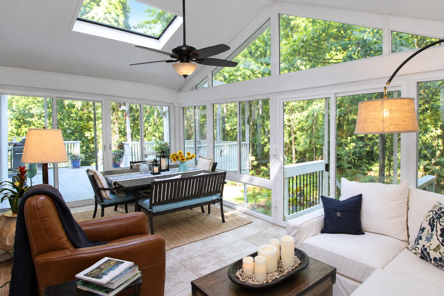 Sunroom interior with white vinyl framing, large windows, skylight, ceiling fan, and dining and lounge furniture.